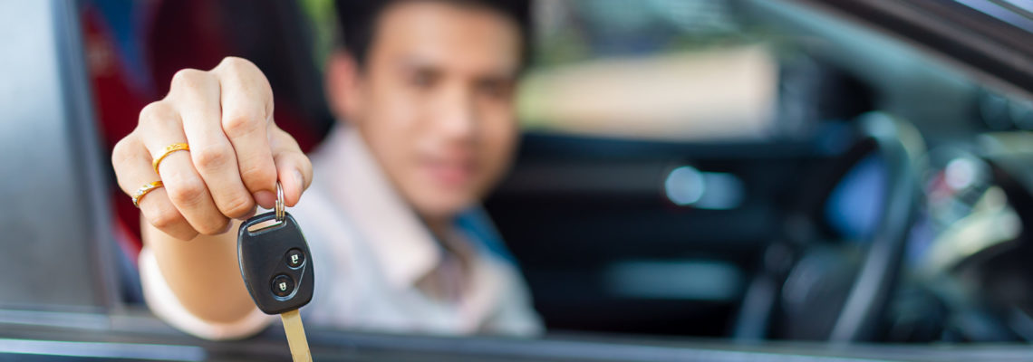 Selective focus on key remote of car in hand of handsome man with blurred young man smiling and sitting in the convertible car